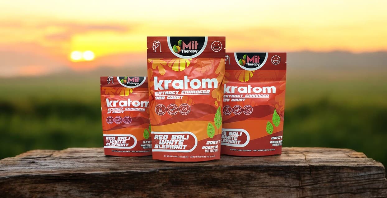 Three packages of Mit Therapy Red Bali + White Elephant capsules sit on a wooden surface against a serene sunset backdrop, highlighting the allure of Mit Therapy's Red Bali blend.