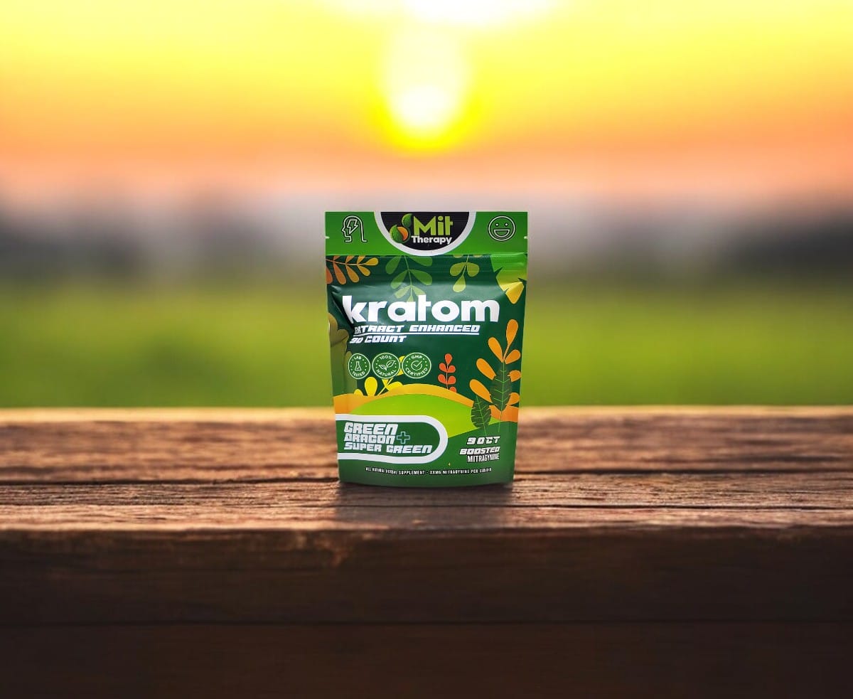 A package of Mit Therapy Green Dragon + Super Green Capsules, known for its high potency, is displayed on a wooden surface. The packaging combines green and yellow hues, set against a blurred outdoor scene with a vibrant sunset in the background.