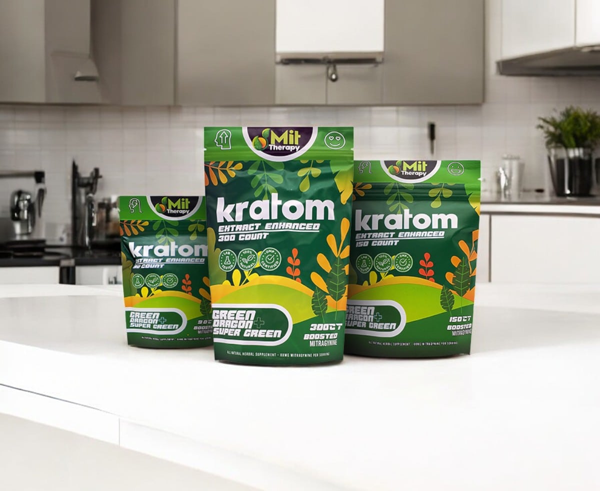 Three green and orange packages of Mit Therapy Green Dragon + Super Green Capsules kratom products are displayed on a white kitchen counter.