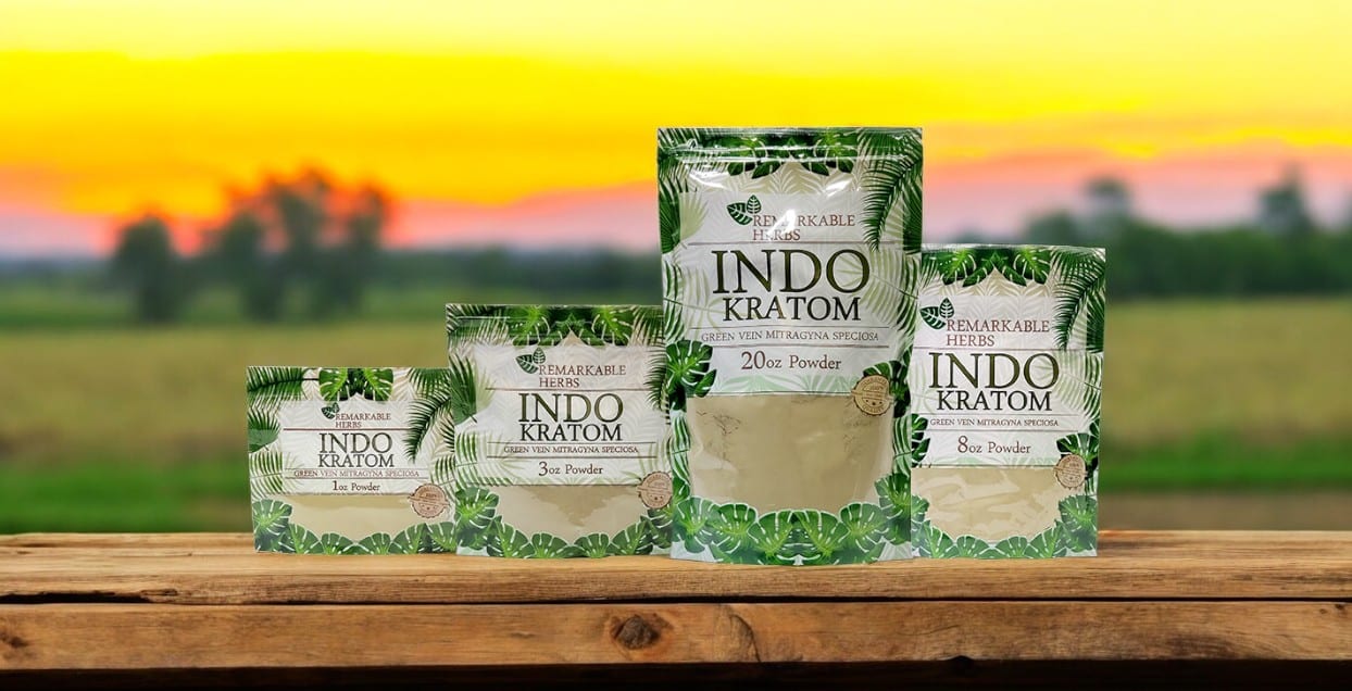 The packaging of Remarkable Herbs Kratom Indo Powder is beautifully showcased on a wooden surface, complemented by a softly blurred outdoor sunset in the background.