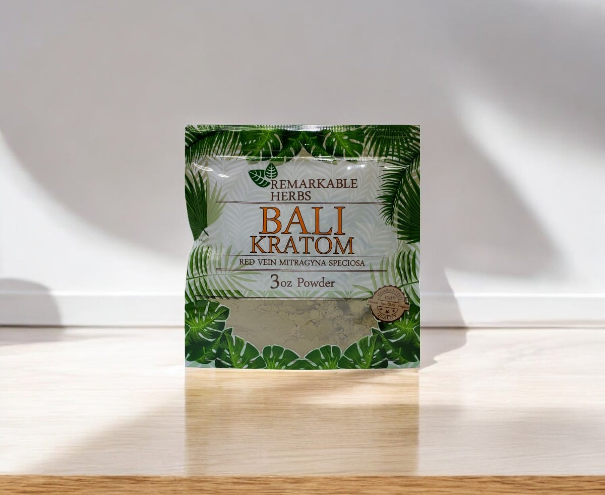 A 3 oz package of Remarkable Herbs Red Bali Kratom Powder sits on a wooden surface, casting a subtle shadow in the background.