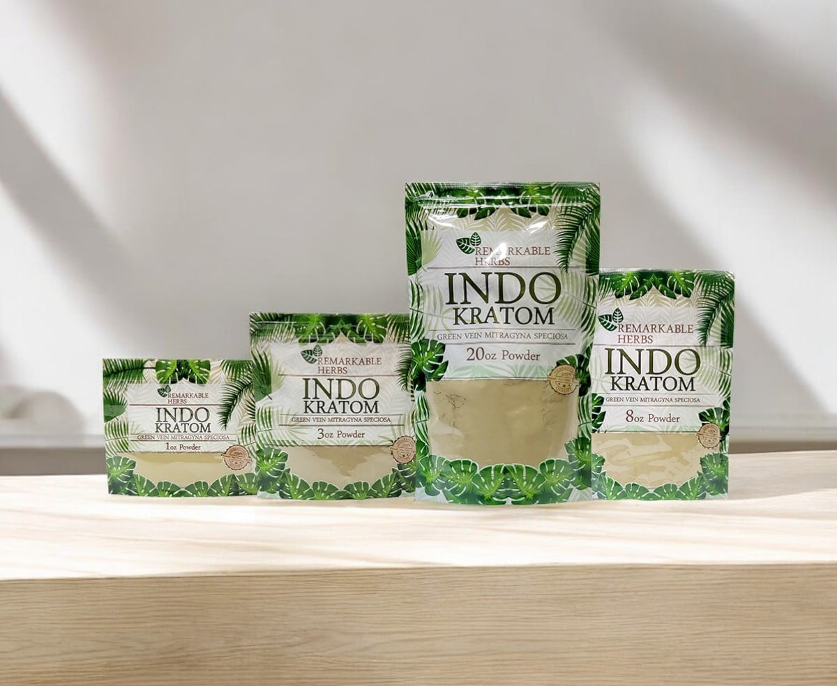 Four green and white packages labeled "Remarkable Herbs Kratom Indo Powder," featuring the remarkable Indo powder in varying sizes, are displayed on a light wooden surface.